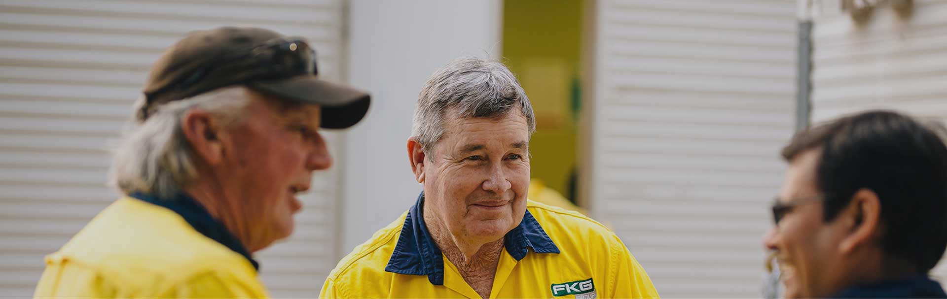 Three male FKG personnel wearing high vis FKG branded uniforms, discussing a project on site